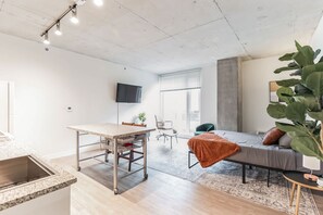 A modern living space with a kitchen area, a dining table, a sofa, and a large plant. - 2  New Studios with Stunning City Views (Cleveland)