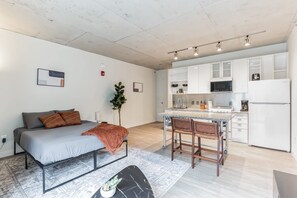 A modern apartment with a grey sofa, a small dining table, and a kitchen with white cabinets and appliances. - 2  New Studios with Stunning City Views (Cleveland)