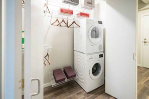 A compact laundry room with a stacked washer and dryer, a drying rack, and a small shelf with boxes. - 2  New Studios with Stunning City Views (Cleveland)