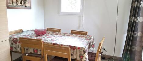 A dining area with a table covered by a patterned tablecloth, surrounded by wooden chairs.