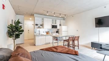 Eine moderne Wohnung mit Küchenzeile, einem Essbereich, einem Wohnzimmer mit Sofa und Fernseher sowie einem großen Fenster.