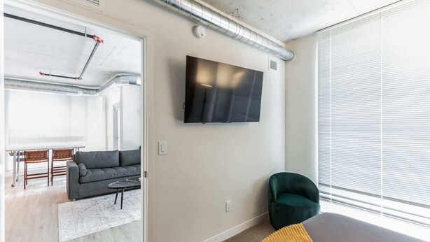 Ein modernes Wohnzimmer mit einem grauen Sofa, einem grünen Sessel und einem flachbildfernseher an der Wand.
