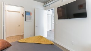 Ein Schlafzimmer mit Bett, einem an der Wand befestigten Fernseher und einer Tür zu einem anderen Raum.