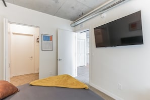 Un dormitorio con cama, televisor montado en la pared y puerta que da a otra habitación.