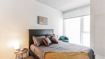 A modern bedroom with a bed, bedside lamp, and a window with blinds.