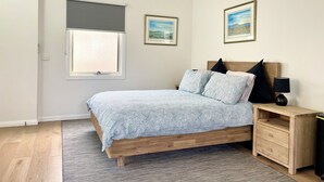 A bedroom with a wooden bed, a nightstand, a lamp, a window with a blind, and two framed pictures on the wall.