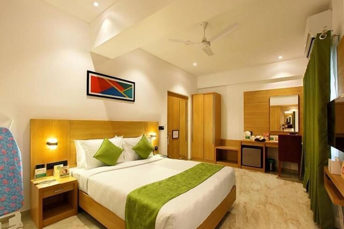 A hotel room with a bed, bedside table, lamp, wardrobe, mirror, and a television.