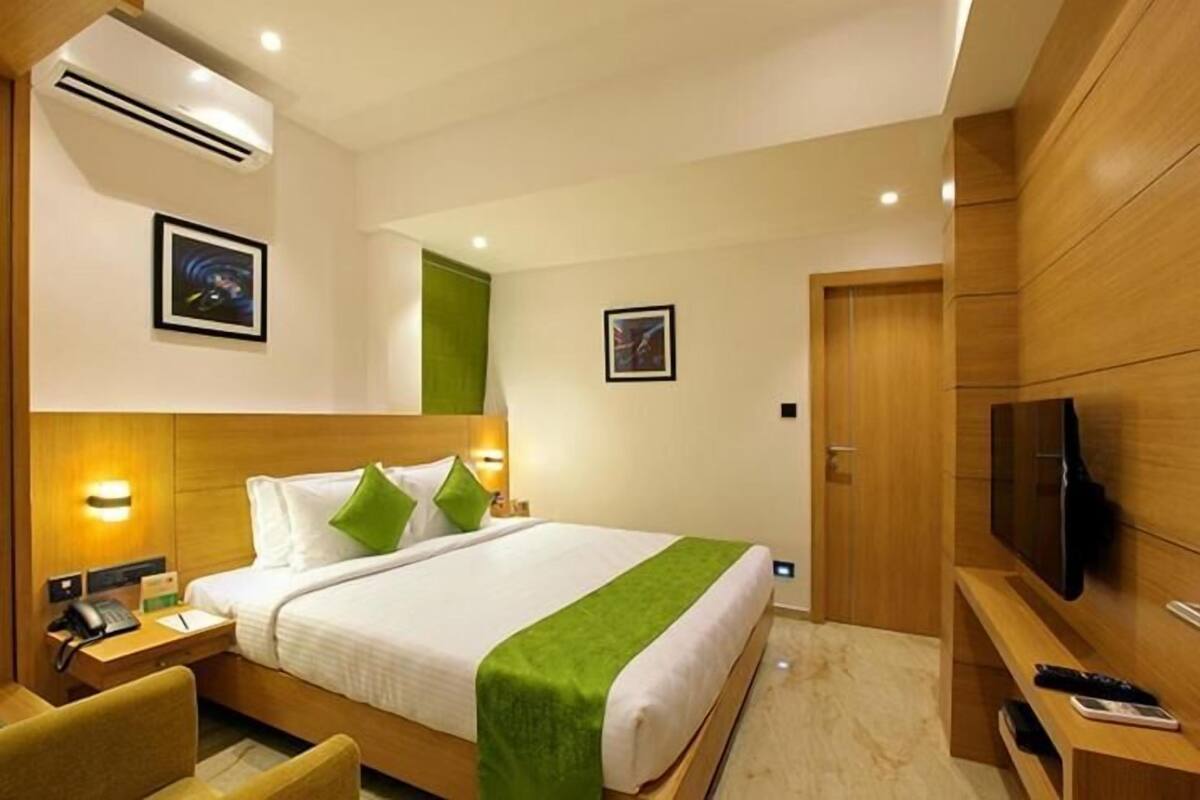 A hotel room with a bed, a TV, a desk with a phone, and a chair.