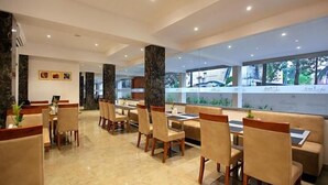 A modern dining area with marble flooring, wooden chairs, and tables. There are large windows with a view of greenery outside. - PARK RESIDENCY KODUNGALLUR (Kodungallur)