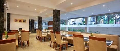 Un comedor moderno con suelo de mármol, sillas y mesas de madera. Amplias ventanas ofrecen vistas a zonas verdes.