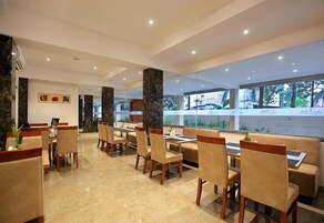 Un comedor moderno con suelo de mármol, sillas y mesas de madera. Amplias ventanas ofrecen vistas a zonas verdes.