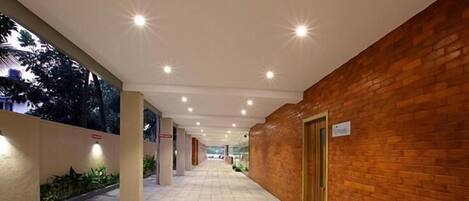 A corridor with tiled flooring, a brick wall on one side, and a door at the end.