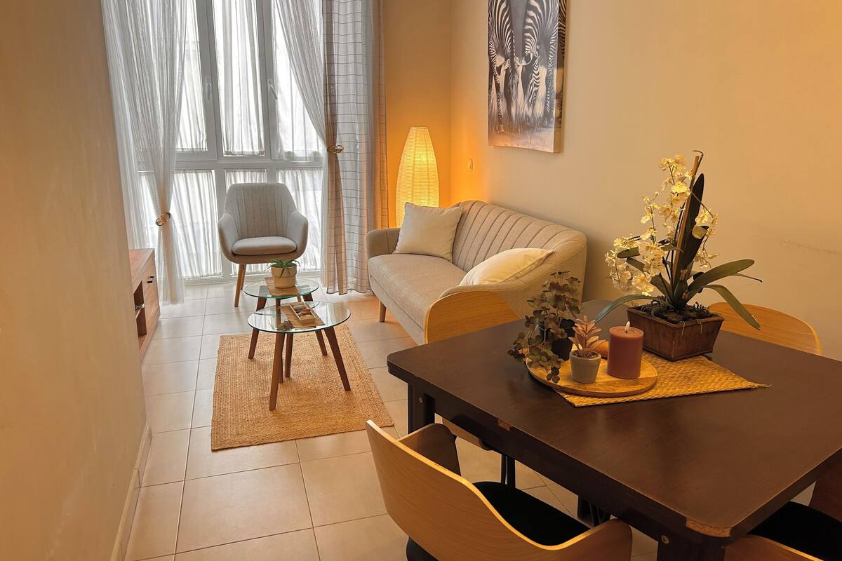 Una sala de estar moderna con un sofá, una mesa de comedor con sillas, una mesa de centro de vidrio y una planta en maceta.