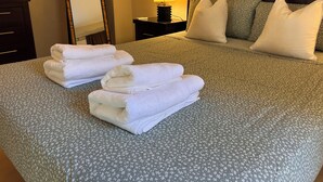 Uma cama bem arrumada com toalhas brancas dobradas, uma luminária de mesa e um espelho em um criado-mudo.