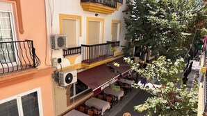 Um restaurante com mesas ao ar livre, uma varanda com guarda-corpo e uma árvore em primeiro plano.
