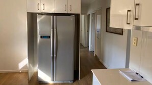 A modern kitchen with a stainless steel refrigerator, white cabinets, and a wooden floor.