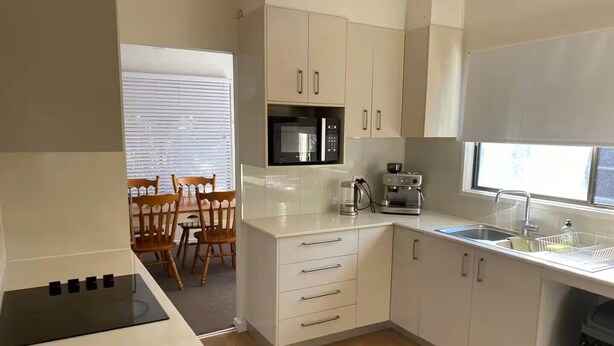 A modern kitchen with white cabinets, a microwave, a coffee maker, and a sink.