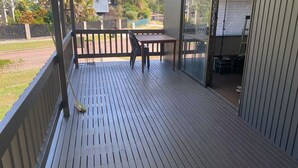 A wooden deck with a table and chairs, a glass door leading to a covered area, and a view of a residential street.