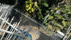 A white metal fence with vertical bars and decorative finials, surrounding a pool area with blue and white tiles.
