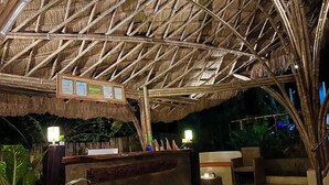 A thatched-roof reception area with a wooden counter, two illuminated signs, and tropical plants. - La Colonial Resort (El Nido)