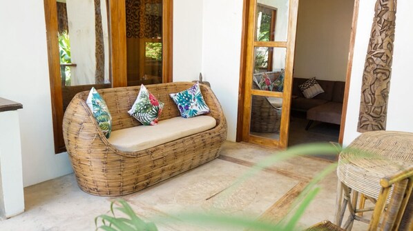 A wicker sofa with cushions, a wooden door, and a view of a garden. - La Colonial Resort (El Nido)