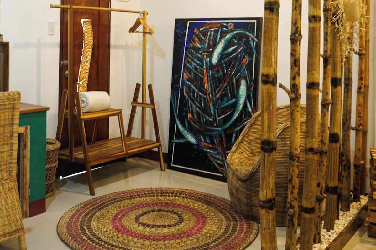 Una habitación con un cuadro grande, una lámpara de pie, una silla tejida y una estructura de bambú.
