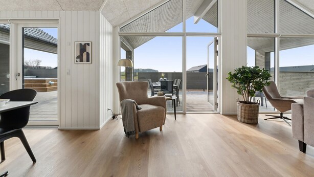 Amplia sala de estar con un gran ventanal corredero que da a un patio exterior. En el interior, hay dos sillones, una mesa de comedor con sillas y una planta en maceta.
