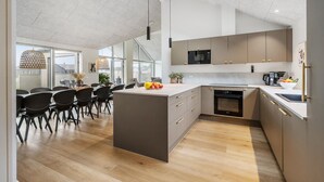 Una cocina moderna con una isla central, electrodomésticos integrados y una zona de comedor con sillas negras e iluminación colgante.
