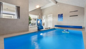 Una piscina interior con un tobogán azul, una zona de estar y un cartel de VitaVilla en la pared.