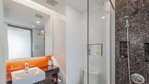 Een moderne badkamer met een douchecabine van glas, een witte wastafel met spiegel erboven en een donker houten wastafelmeubel.