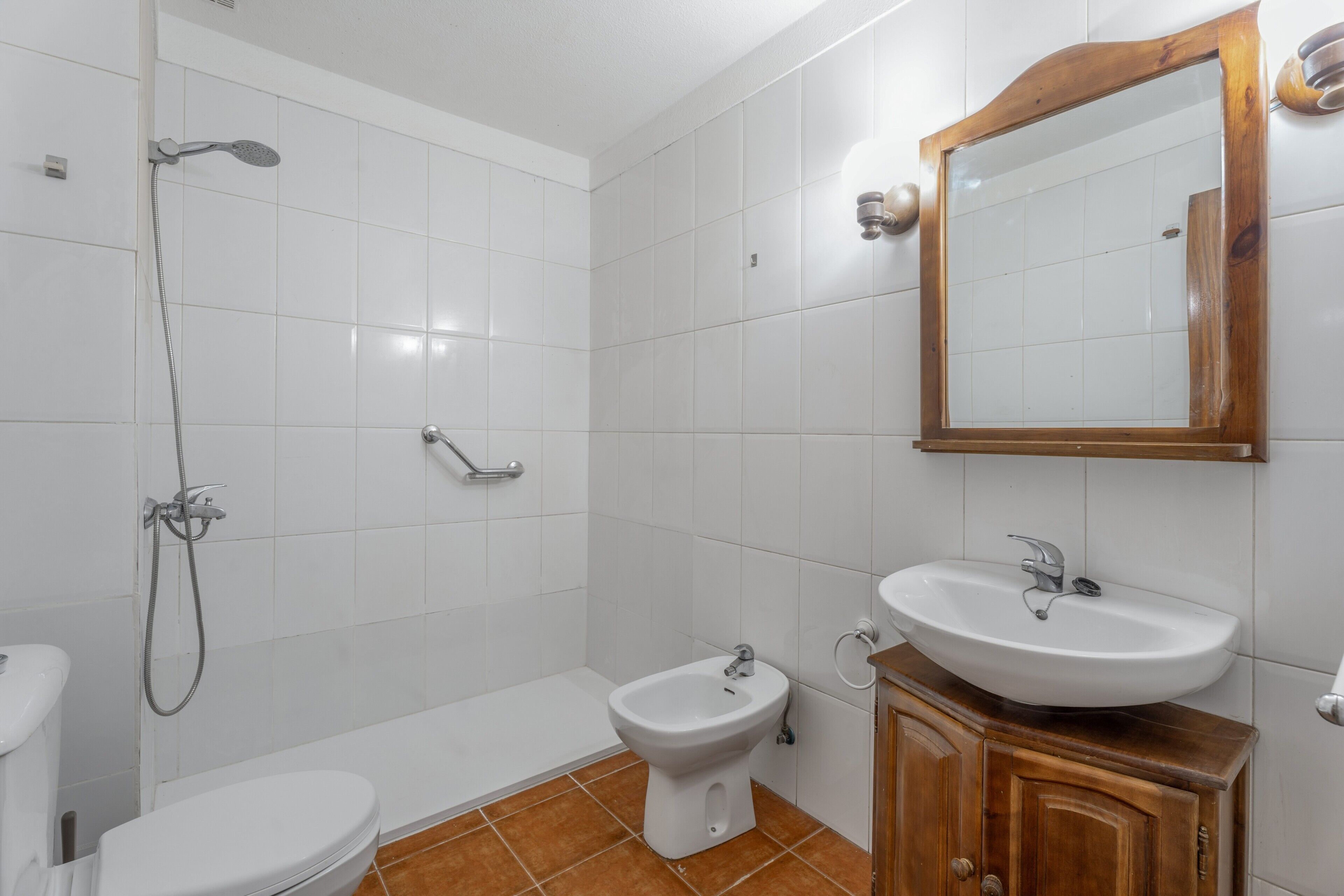 Un baño con inodoro, bidé, ducha, lavabo y un armario de madera.