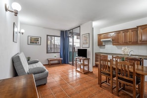 A compact living space with a sofa, a dining table with chairs, a TV on a stand, and wooden cabinets.