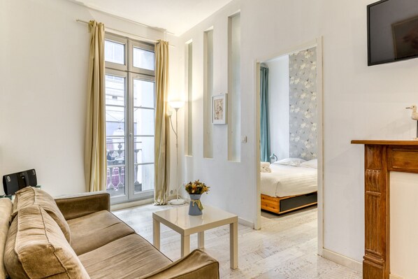A modern living room with a sofa, a small table, and a bed in the background. - City Balcony (Montpellier)