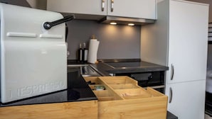 A kitchen with a white espresso machine, wooden drawers, and white cabinets. - JH Apartments Nittenau | Design Studio (Nittenau)