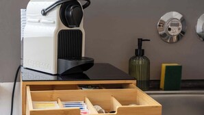 A coffee machine on a wooden table with a drawer below containing various items. - JH Apartments Nittenau | Design Studio (Nittenau)