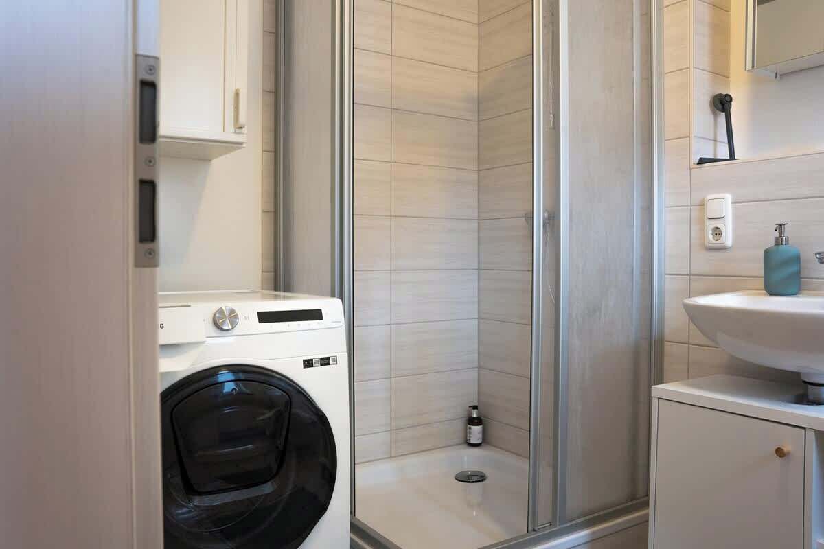 Ein kleines Badezimmer mit Waschmaschine, Duschbereich und Waschbecken.