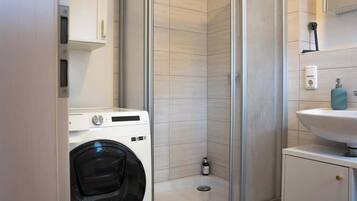 Ein kleines Badezimmer mit Waschmaschine, Duschbereich und Waschbecken.