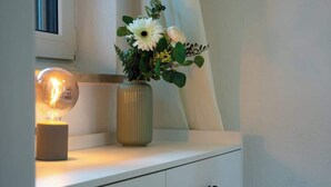 A bedside table with a lamp and a vase of flowers. - JH Apartments Nittenau | Design Studio (Nittenau)