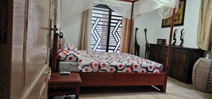 Een slaapkamer met een bed, nachtkastje en een raam met een geometrisch patroon.