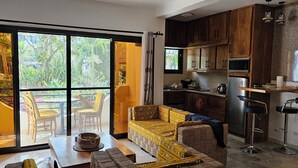 A modern kitchen with wooden cabinets, a dining area with a table and chairs, and a sliding glass door leading to a balcony with outdoor furniture. - Apartment Saly 3ch - 3sb - Swimming pool - Beach - Veranda (Saly)
