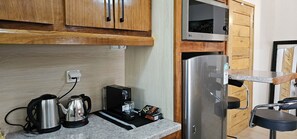 Una kitchenette compacta con armarios de madera, hervidor de acero inoxidable, cafetera y refrigerador.
