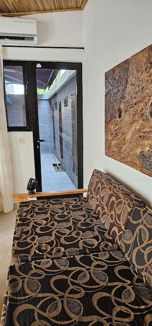 Una habitación con cama, ventilador de techo, puerta que da a un pasillo y un cuadro grande en la pared.