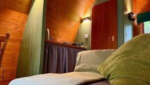 A cozy cabin interior with a bed, wooden walls, a small kitchenette, and a window. - Aelfred Pod (West Stow)