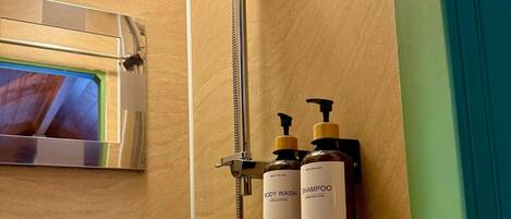 A bathroom with a shower, a sink, and two bottles of body wash and shampoo.