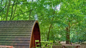A wooden structure with a bench and two chairs outside, surrounded by trees. - Wulfrun Pod (West Stow)