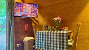 A cozy wooden interior with a television displaying a scenic view, a table set with a checkered tablecloth, and a vase of flowers. - Wulfrun Pod (West Stow)