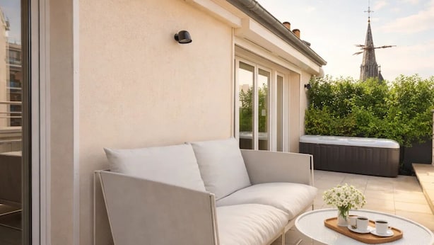 An outdoor seating area with a sofa and a small round table, a hot tub, and a view of a church spire. - 1530 Roux (Paris)