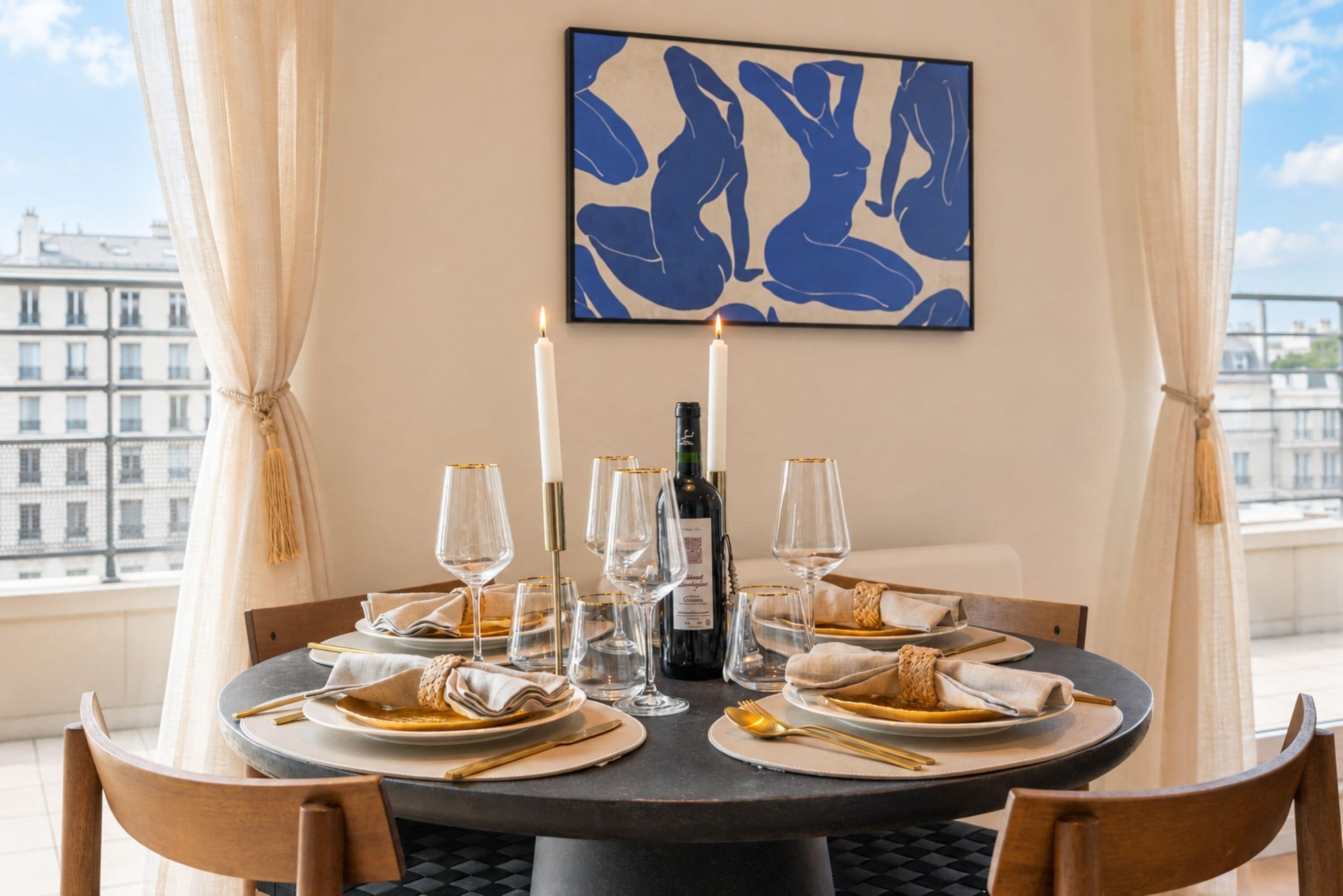 Une table ronde dressée pour le dîner, avec une bouteille de vin, des verres et des couverts.