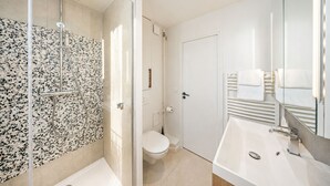 A modern bathroom with a glass-enclosed shower, a toilet, and a sink with a mirror. - 1530 Roux (Paris)