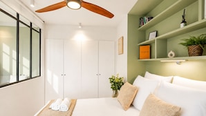 A bedroom with a bed, a ceiling fan, a window, and a green wall with shelves. - 1530 Roux (Paris)